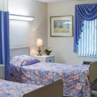 A cozy room with two beds, adorned with patterned bedspreads, a lamp on a nightstand, and a window with blue curtains.
