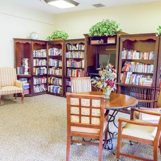 A cozy library room with bookshelves, chairs, and a table for reading.