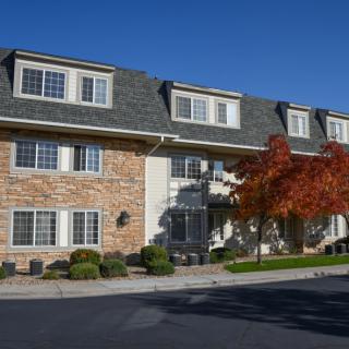 A residential apartment building with a brick exterior, surrounded by autumn foliage under a clear blue sky.