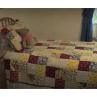 A cozy bedroom with a colorful patchwork quilt and a teddy bear on the bed.