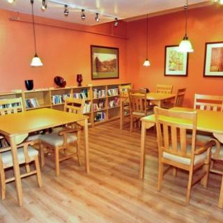 A cozy cafe interior with wooden tables, chairs, and bookshelves against orange walls.