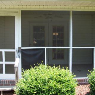A screened porch with a damaged section, surrounded by bushes.