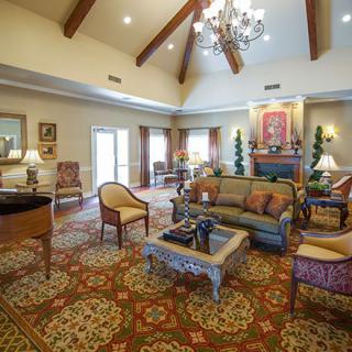 A spacious and elegantly decorated living room with a high ceiling, featuring a chandelier, comfortable seating arrangements, and warm lighting.