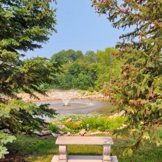 A peaceful garden scene with a bench overlooking a fountain surrounded by lush greenery.