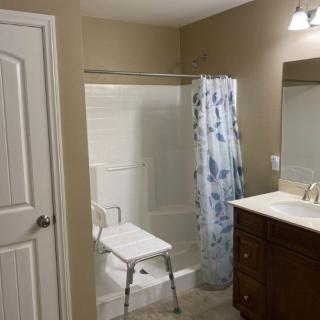 A bathroom with a shower stall, a white chair, and a sink with a mirror above it.