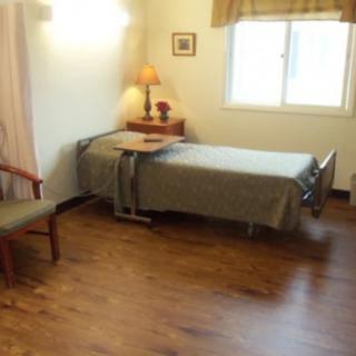A simple room with a hospital bed, wooden flooring, and a window with curtains.