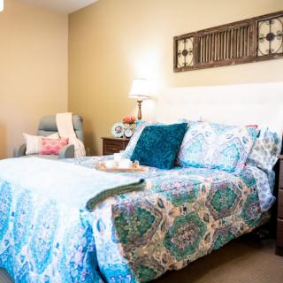 A cozy bedroom featuring a colorful bedspread, pillows, and a bedside lamp.