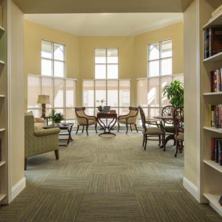 A cozy library reading area with comfortable chairs, large windows, and bookshelves.