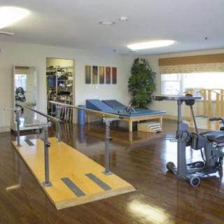 A well-equipped physical therapy room with exercise equipment and therapy beds.