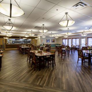 An empty restaurant interior with wooden tables and chairs, featuring elegant lighting and wood flooring.
