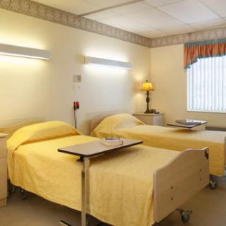 A clean and well-organized hospital room with two beds and a window letting in natural light.
