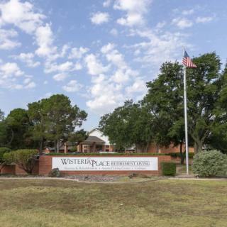 A view of a school entrance featuring a sign, trees, and an American flag on a flagpole.