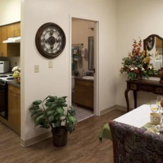 A cozy apartment interior featuring a kitchen and dining area with decorative elements like a wall clock, plants, and a mirror.