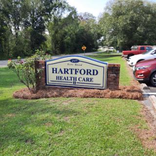A sign indicating Hartford Health Care, surrounded by greenery and parked cars.