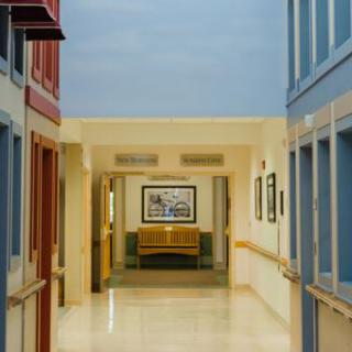 A serene and spacious hallway featuring a waiting area with a bench, framed artwork, and soft lighting.
