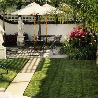 A tranquil garden patio with seating, an umbrella, statues, and lush greenery.