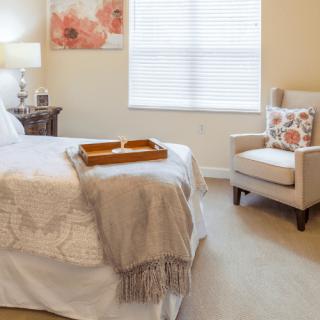 A cozy bedroom with a neatly made bed, an armchair, and soft lighting.