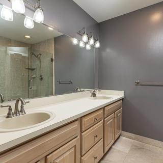 A modern bathroom with a large mirror, dual sinks, and a spacious shower area.