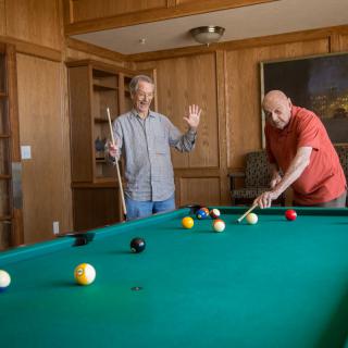 Two people playing billiards on a pool table indoors.