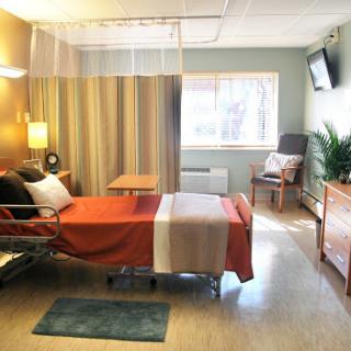 A modern hospital patient room featuring a bed, seating area, and natural light.