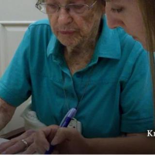 An elderly person receiving assistance with writing from a younger individual.