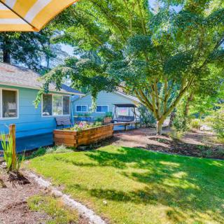 A sunny backyard featuring a well-kept garden and lush grass, surrounded by trees with a view of the house.