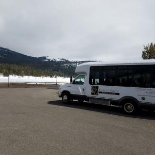 A tour bus parked in a lot with snowy mountains in the background under a cloudy sky.