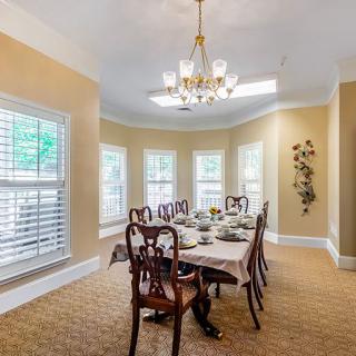 An elegant dining room with a large table, chairs, and a chandelier, surrounded by multiple windows.