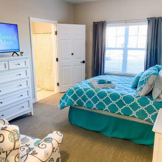 A cozy bedroom with turquoise bedding, a dresser with a TV, and a large window.