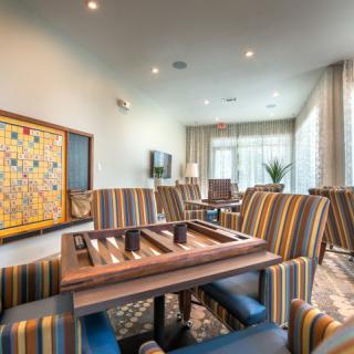 A modern living room featuring a backgammon board on a table surrounded by striped chairs.