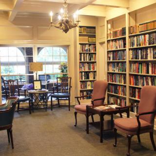 A cozy library reading room with bookshelves, comfortable chairs, and large windows.