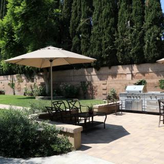 A sunny backyard patio with an umbrella, seating area, and grill.