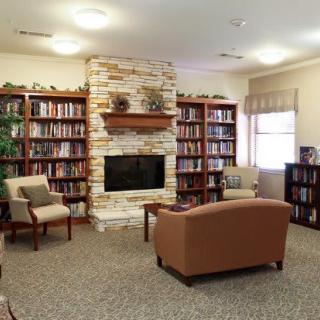 A cozy library room with bookshelves, a stone fireplace, and comfortable seating.