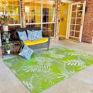 A cozy patio setup with rattan furniture, adorned with a vibrant green rug featuring tropical leaf patterns.