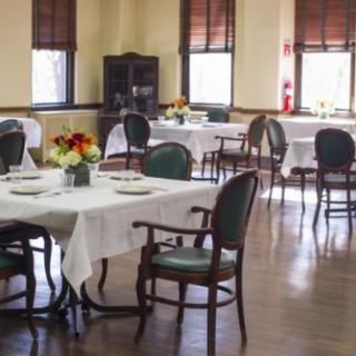 A cozy dining room with elegantly set tables and chairs, featuring floral centerpieces.