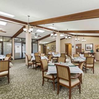A spacious dining room with neatly arranged tables and chairs, featuring elegant lighting and a carpeted floor.