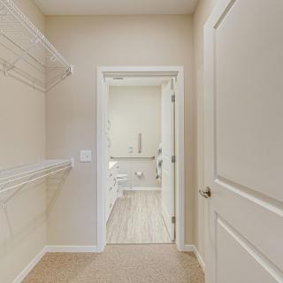 An empty walk-in closet with shelving leading to a bathroom.