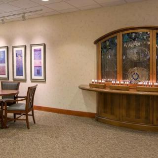 A well-decorated interior room featuring a round table with chairs, framed artwork on the walls, and a wooden shelf adorned with lit candles.