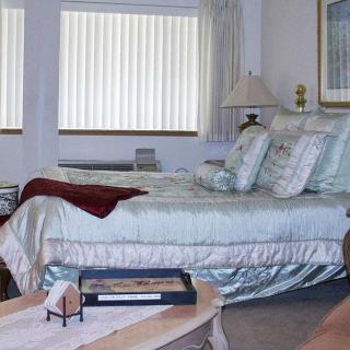 A cozy bedroom interior with a neatly made bed, decorative pillows, and a lamp by the window.