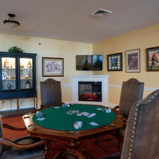A cozy game room featuring a poker table with cards, surrounded by leather chairs and decorated with framed artwork and a fireplace.