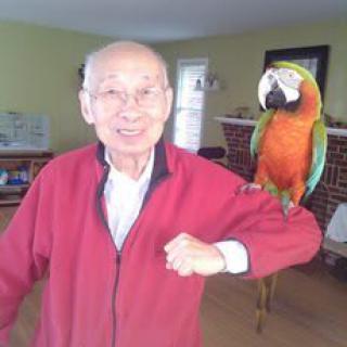 A smiling man with a parrot on his shoulder indoors.