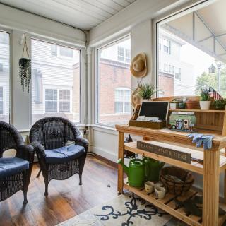 A cozy sunroom with wicker chairs and a small workstation, filled with natural light and greenery.