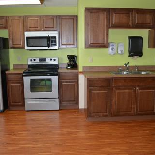 A modern kitchen with wooden cabinets, green walls, and various appliances including a stove, microwave, refrigerator, and coffee maker.