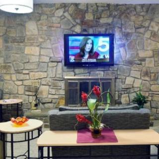 A modern living room with a stone wall, featuring a mounted television and elegant flower arrangements.