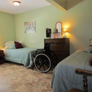 A cozy bedroom with two twin beds, a wheelchair beside a dresser, and soft green walls.