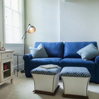 A cozy living room with a blue sofa, stylish ottomans, and soft lighting.