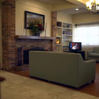 A cozy living room featuring a brick fireplace, a sofa facing a television, and bookshelves for storage.
