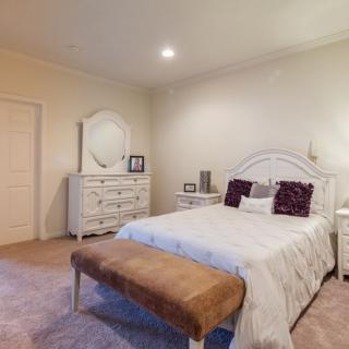 A cozy bedroom with a neatly made bed, white dresser with a mirror, and decor accents.