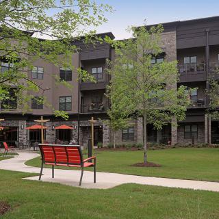 A modern apartment building with a well-maintained outdoor area featuring benches and lush greenery.