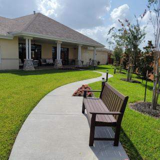 A peaceful backyard scene featuring a walkway, bench, and well-maintained lawn.